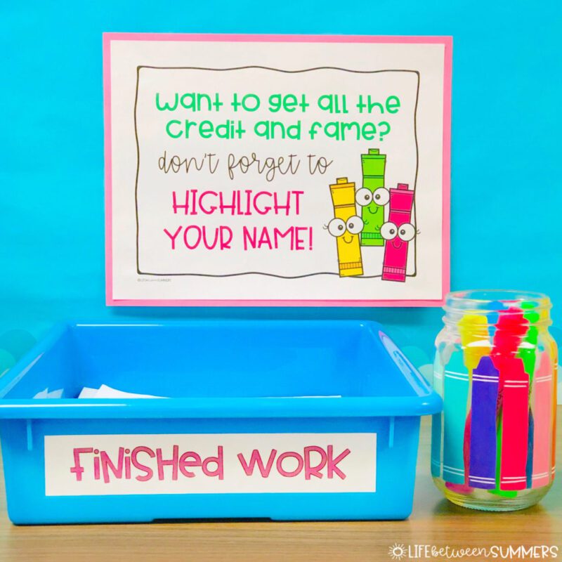 a blue bin labelled finished work next to a jar with highlighters under a sign reminding students to highlight their name on their papers