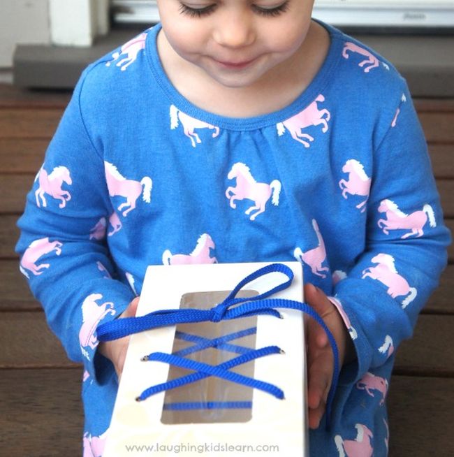 Toddler holding a shoe made from a tissue box and shoelaces