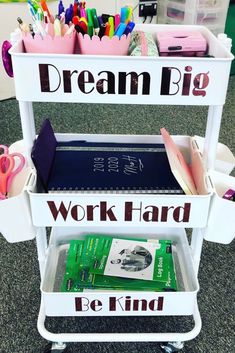 A white rolling cart with three shelves is shown. The first is labled work hard, the second dream big, the third be kind. 