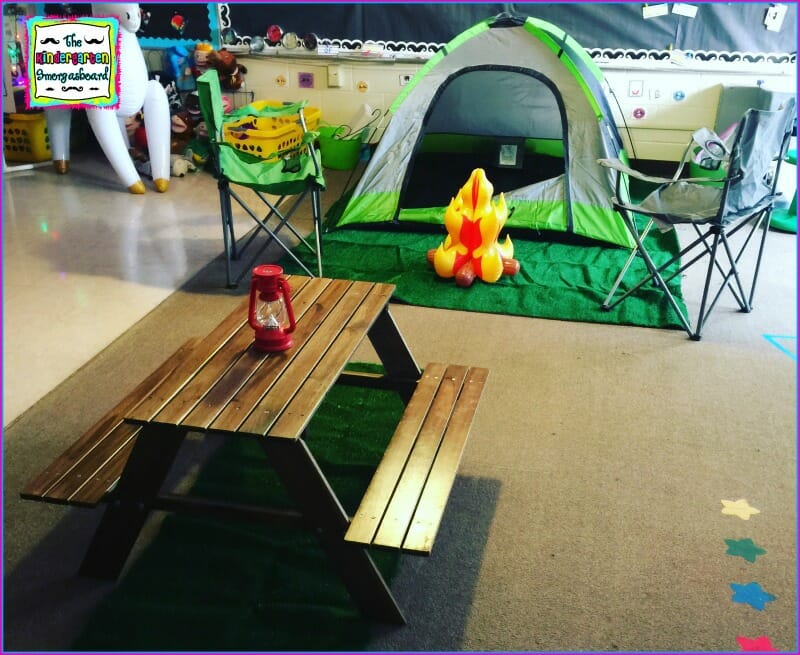 A classroom is shown that has been setup to look like a campsite. A picnic table, a green tent, and an inflatable campfire are shown.