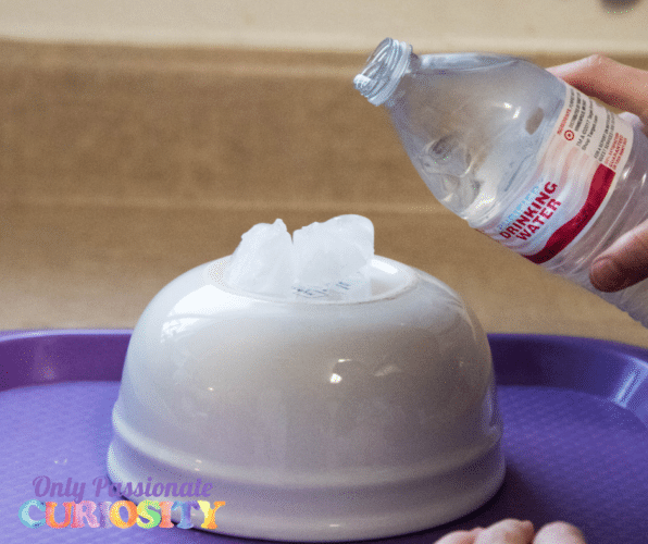 an overturned bowl with ice cubes on top with a child's hand pouring water on top of the ice cubes