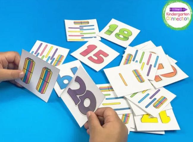 Kindergarten math student holding cards showing the number 20 and bundles of craft sticks equaling 20, with more cards in the background