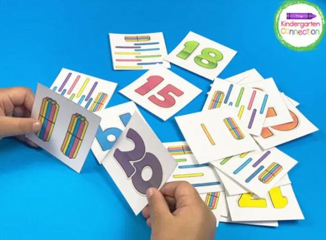 Kindergarten math students holding the cards showing the number 20 and bundles of craft sticks equal 20, and with more cards in the background