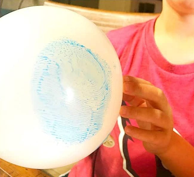 Child holding up a balloon with an enlarged blue fingerprint on it (Kindergarten Science Activities)