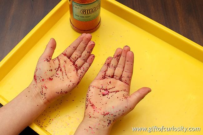 Young student's hands covered in red glitter over a yellow tray