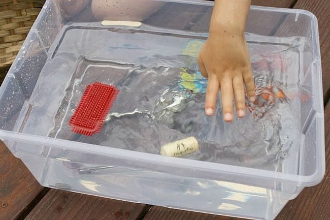 Child's hand placing items in a bin of water to see if they sink or float