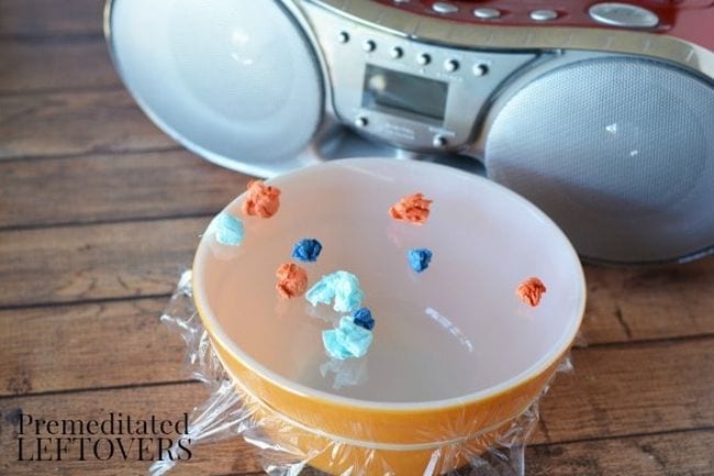 Yellow bowl covered tightly with plastic wrap, with popcorn on top, next to a boom box, as an example of kindergarten science activities