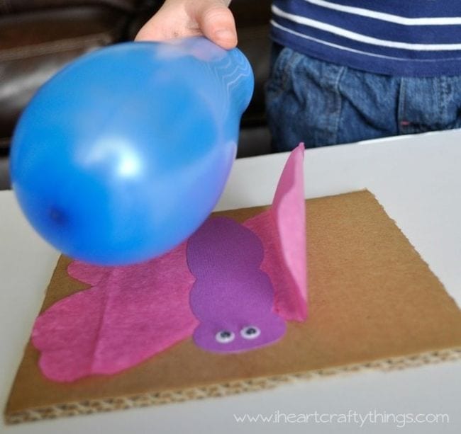 Student's hand holding a blue balloon over a tissue paper butterfly, with wing attracted to the balloon
