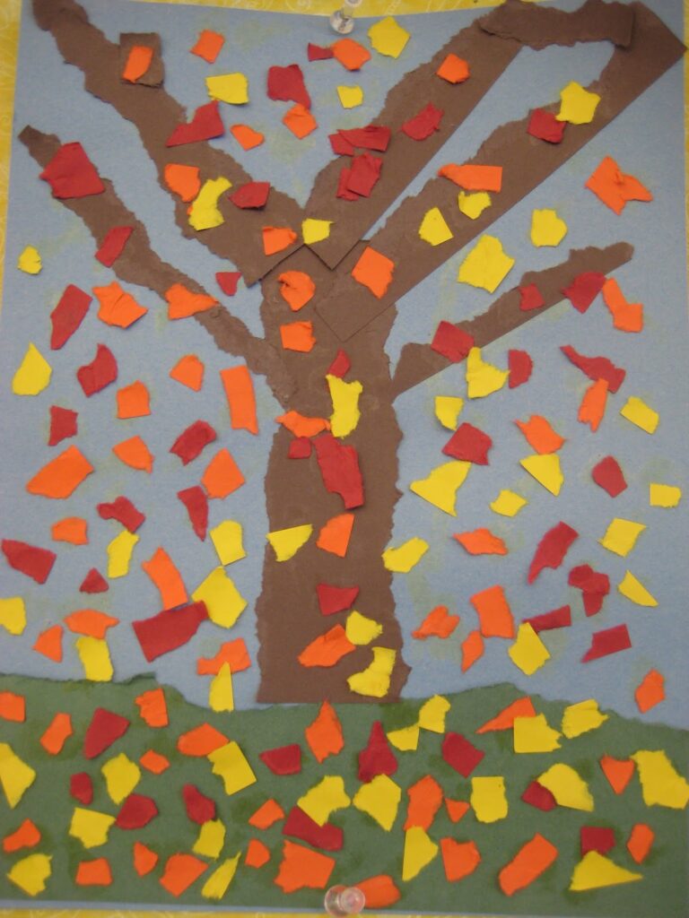 A close up of student art shows a tree with bits of orange yellow and red construction paper all over it to look like falling leaves.