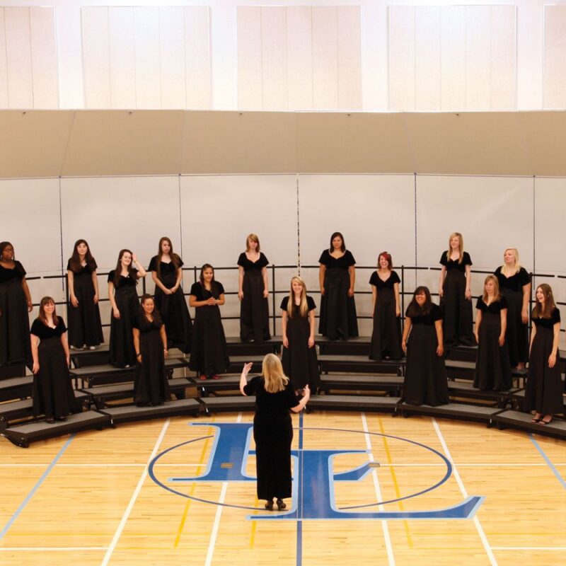 Conductor directing student choir in high school gymnasium with acoustical shell