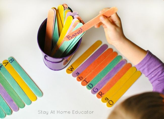 Student pulling a colorful wood craft stick from a pail. Other sticks on the table are labeled with letters. 
