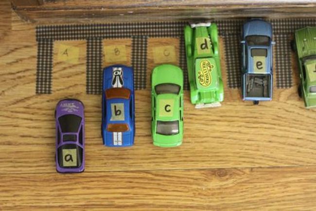 Toy cars labeled with letters of the alphabet, parked in lettered parking spots