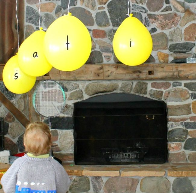 Toddler swatting balloons labeled with letters using a tennis racket