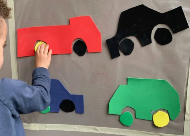 Temas kağıdıyla kaplı bir duvara araba parçalarını bir araya getiren yürümeye başlayan çocuk
