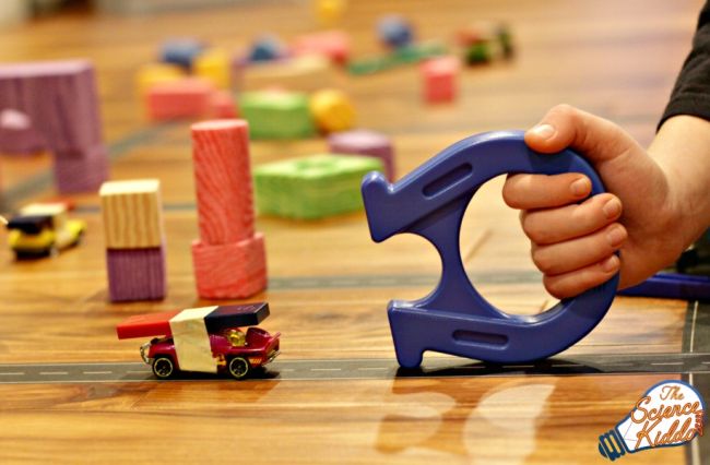 Student using a large magnet to move a toy car with a smaller magnet taped to it (NASCAR Teaching Ideeas)