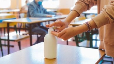 A cropped photo of a person squirting hand sanitizer into their hands in a classroom setting