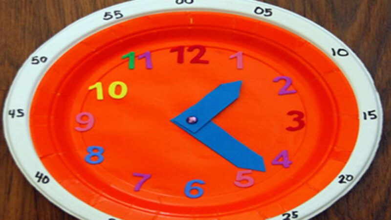 A paper plate is transformed into a clock, there are numbers on the outer edge to indicate the time. 