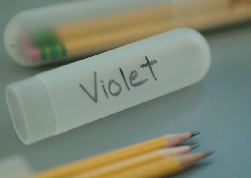 White toothbrush holder filled with pencils and labeled 