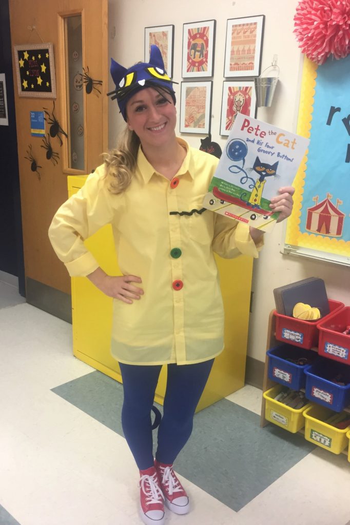 A woman is shown holding a Pete the Cat book.  She is wearing a yellow button up shirt and signature red sneakers.  She is wearing a pet the cat headpiece.