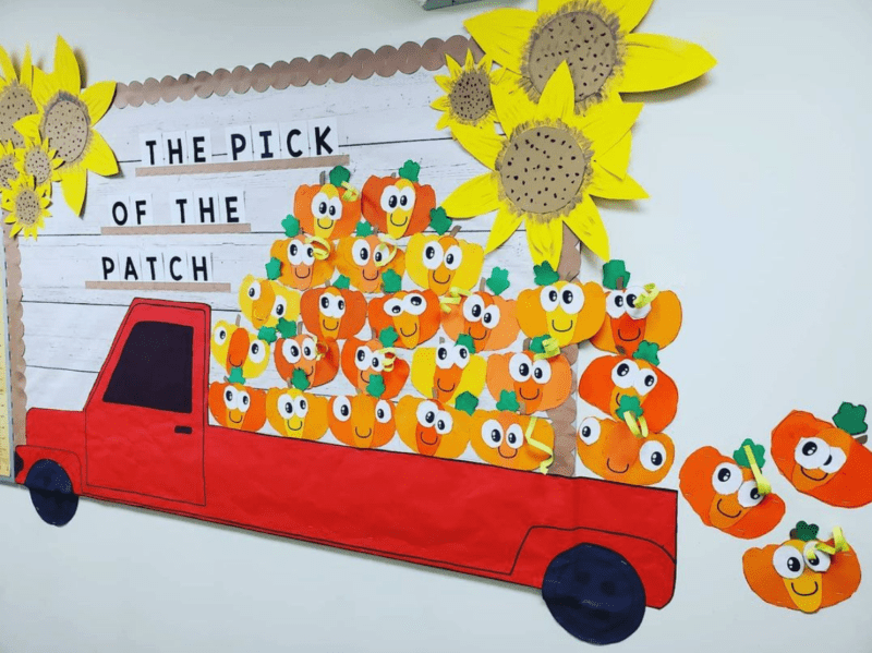 Fall bulletin boards can include a red pickup truck like this one with a bunch of cute cutout pumpkins in the bed with googly eyes. Text reads "The pick of the patch" and there are large sunflowers in the corners.
