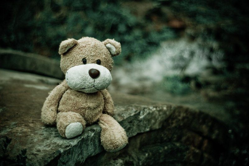 Worn teddy bear sitting on a stone bridge