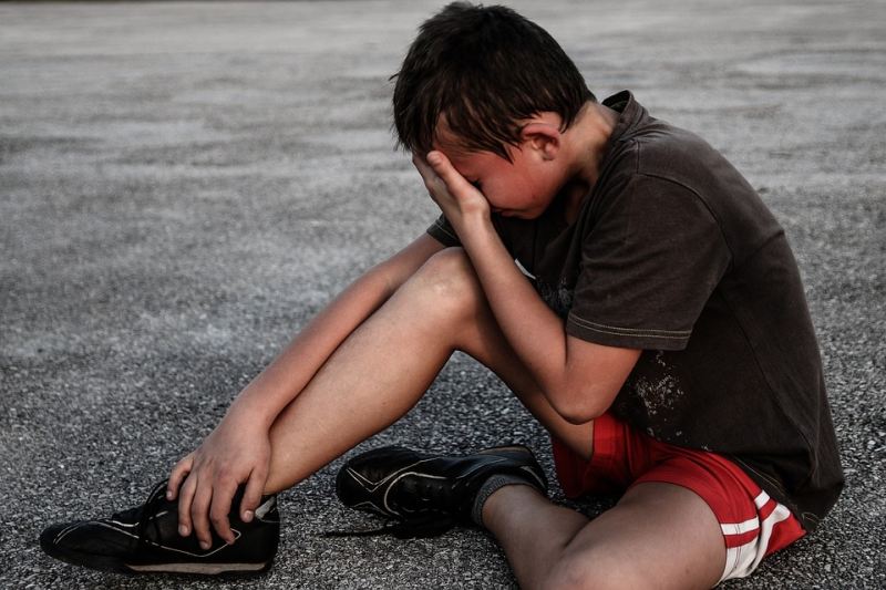 Boy sitting on the ground with his face in his hands