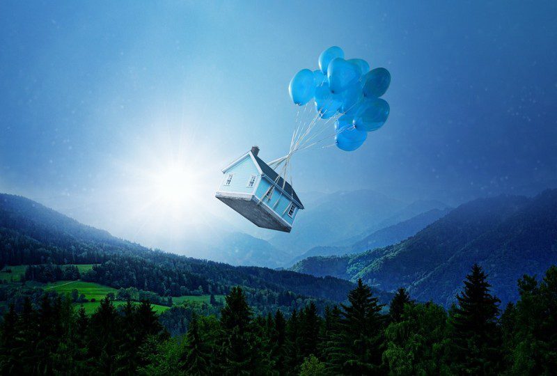 Casa azul flotando en el cielo sobre las montañas, con globos azules