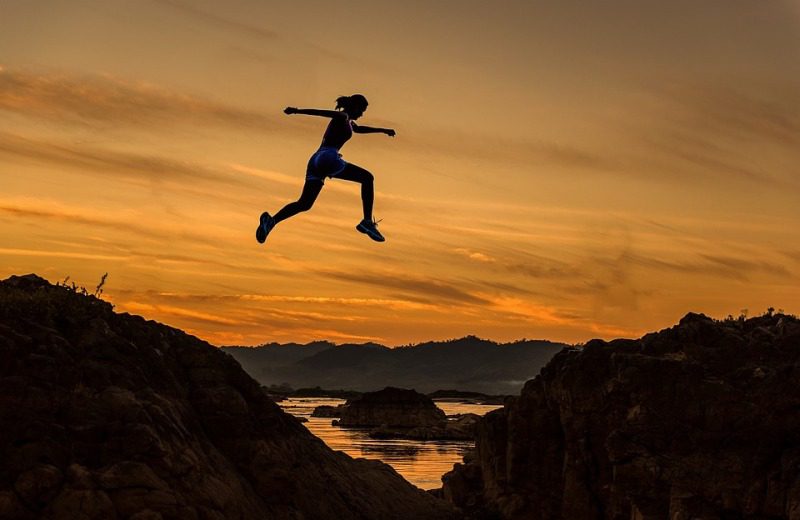Woman leaping across a chasm silhouetted by an orange sky