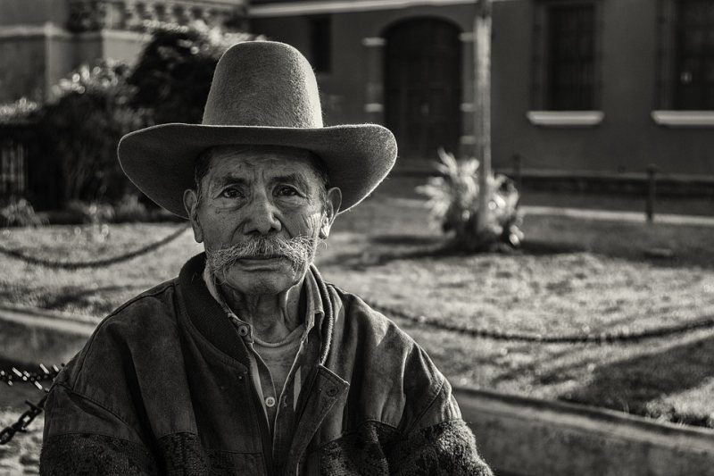 Un anciano con un sombrero de vaquero se sienta frente a una casa (indicación para escribir imágenes)
