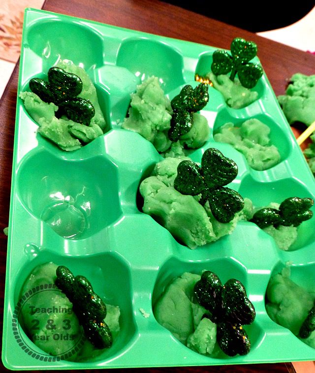 A green bin is separated into sections that are filled with green play dough and sparkly shamrocks (St. Patrick's Day crafts for kids)