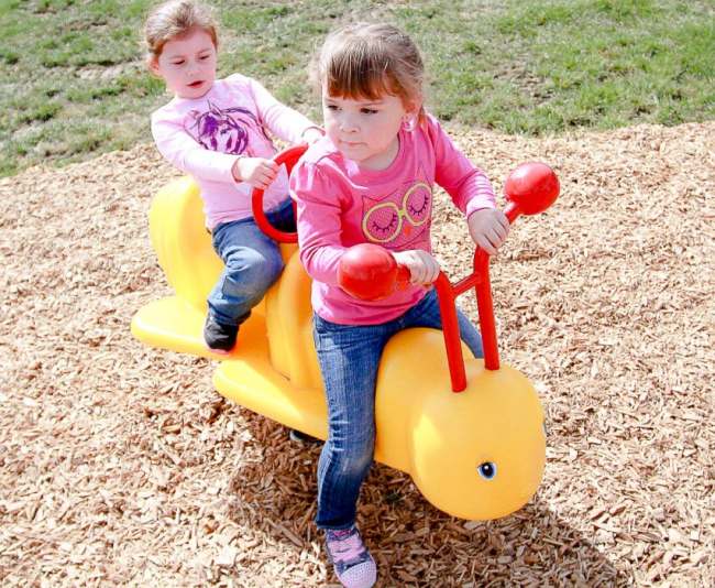 Two preschoolers sitting on a spring toy shaped like a yellow caterpillar (Best Playground Equipment for Schools)