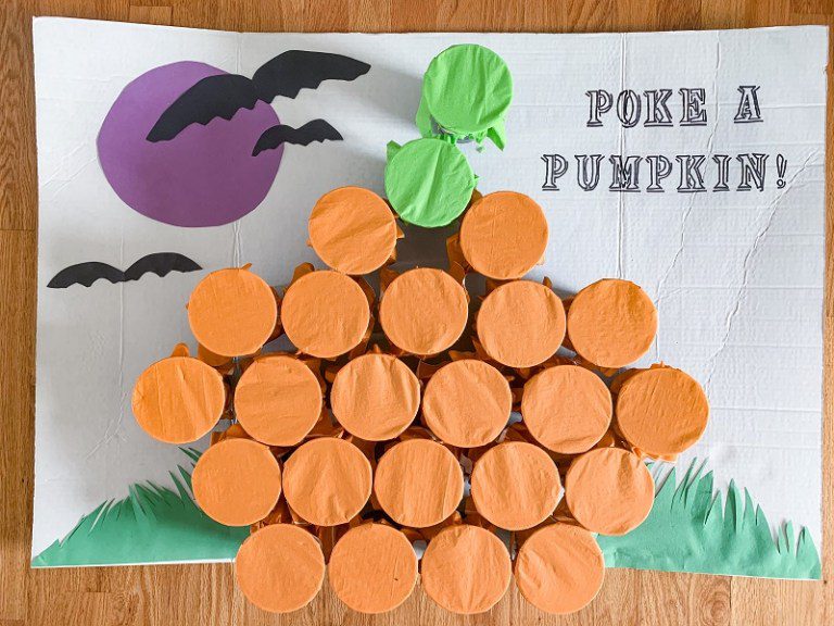 A poster board says Poke a Pumpkin. There is a collection of cups with orange paper over the top to look like pumpkins. The paper can be punctured to reveal what is inside.