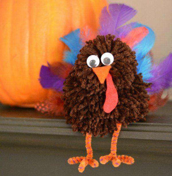 adorable turkey made from pom poms and feathers, as an example of DIY Thanksgiving crafts