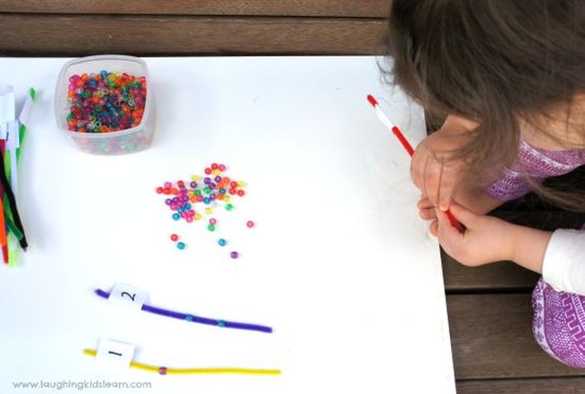 Preschool math student stringing beads onto pipe cleaners