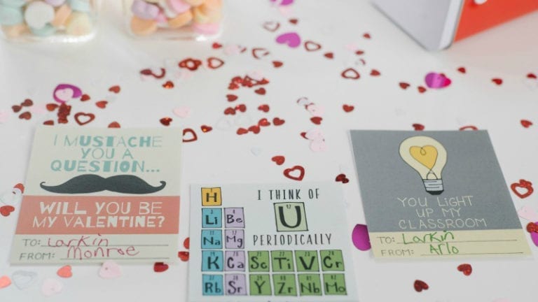 Colorful punny valentines laying on a table covered with mini red hearts