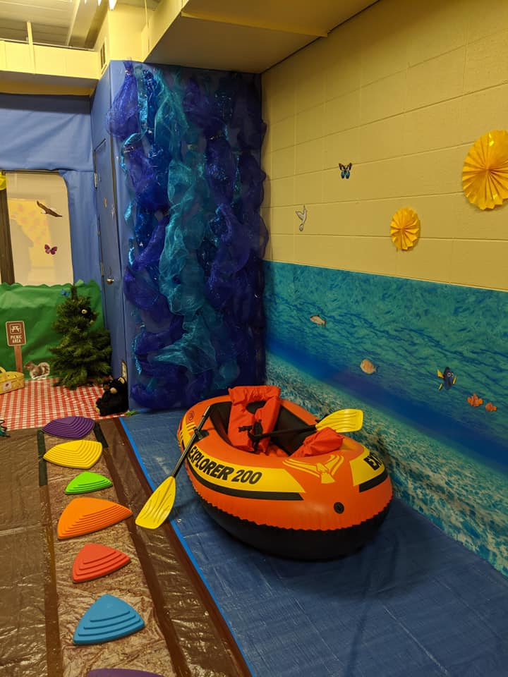 A classroom is setup to look like a river with an inflatable raft and multi-colored stepping stones.