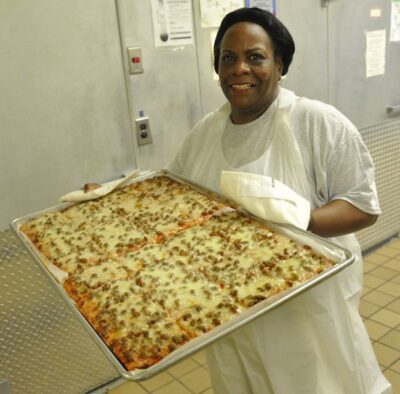 Smiling school lunch lady holding pizza cut into rectangles 