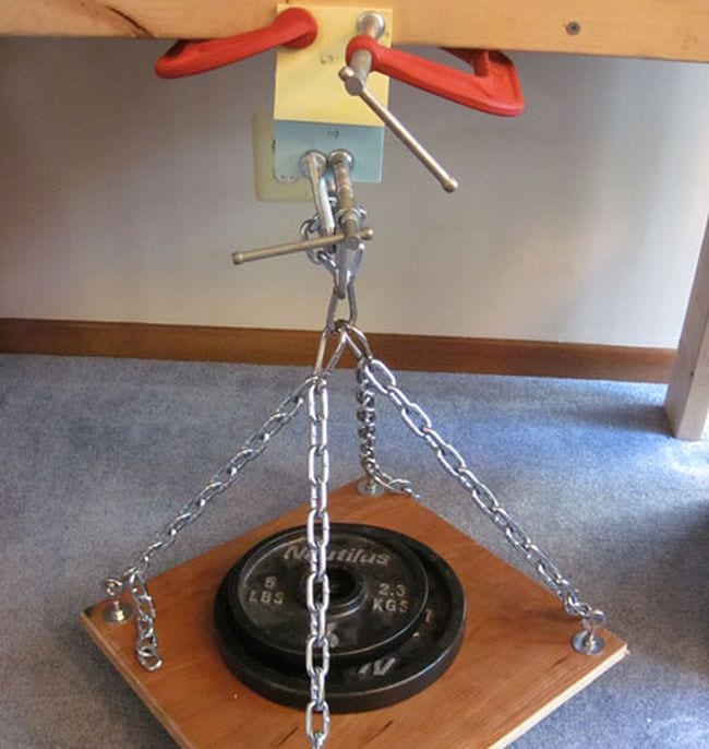 A wood platform holding a weight suspended by chains from two sticky note pads interleaved together (Science Experiments for High School)