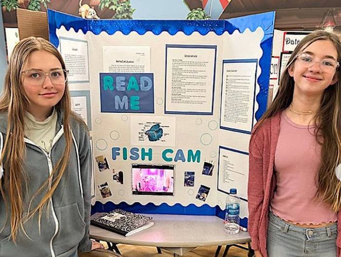 Two middle school girls standing in front of their science fair project board about Fish Cams