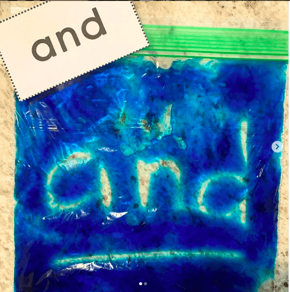 A zip-top bag with blue paint inside with the word "and" traced onto it to match a sight word card
