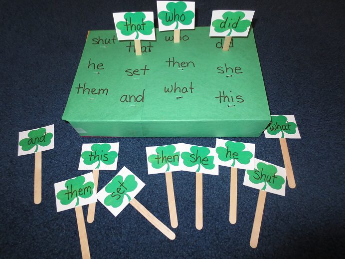 A box is covered with green construction paper and has sight words written on it in black marker. Shamrocks with the sight words are attached to Popsicle sticks and stuck in the box by the correct sight word.