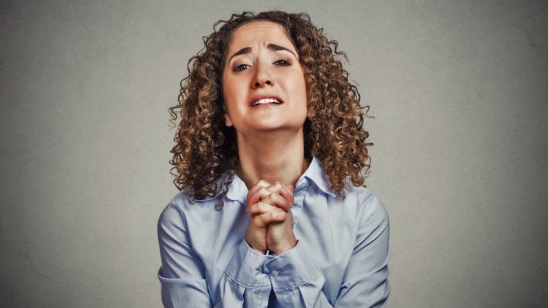 young woman gesturing with clasped hands, pretty please