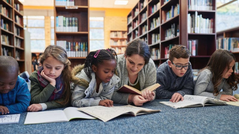 Shot of a group of elementary school kids and their teacher lying down while working in the library