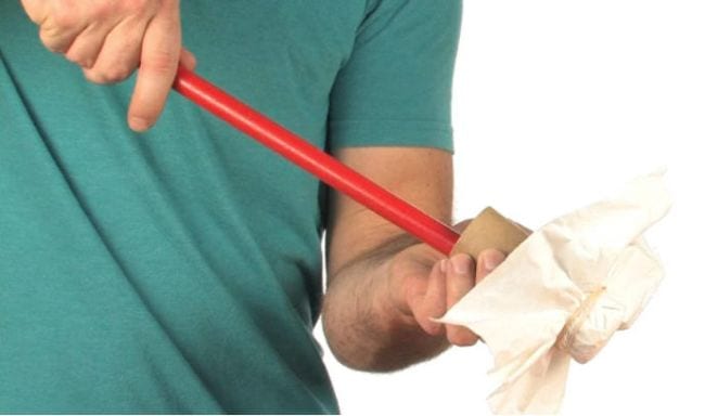 Student pushing a wooden dowel into a toilet paper tube covered in tissue paper at one end