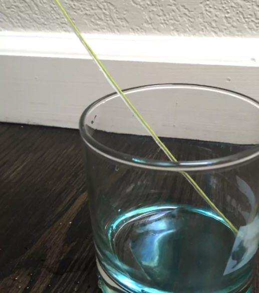 String running down into a glass partially filled with blue water
