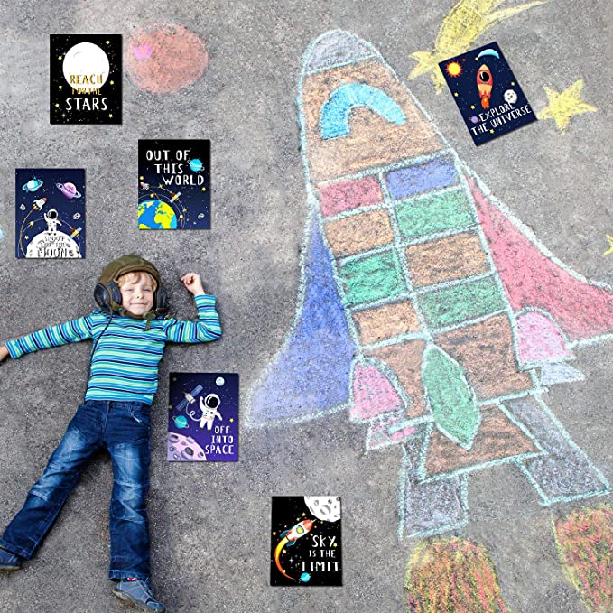 Boy laying down on ground next to space shuttle drawn in chalk and Classroom inspirational posters featuring space theme