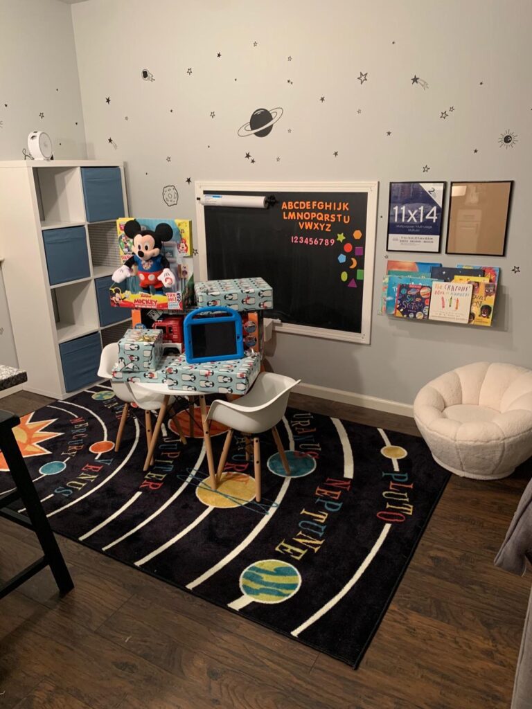 Classroom with space rug, small table, blackboard, book shelf, and toys