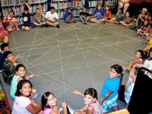 students sitting in a large circle holding yarn to create a large "spider web"