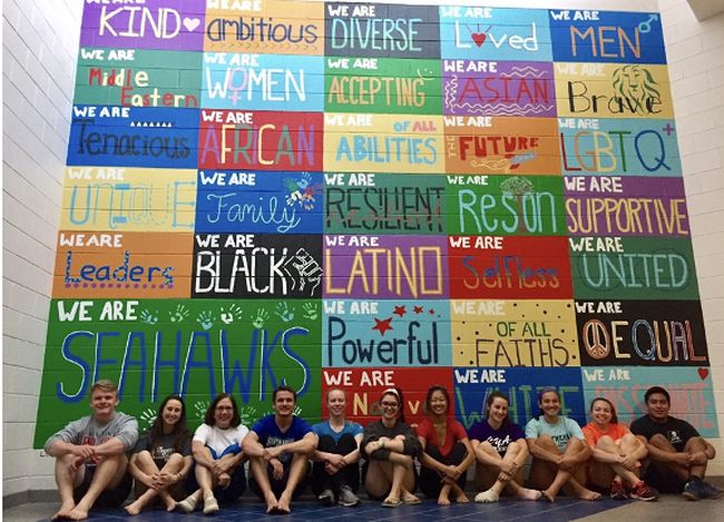 Students sitting in front of a colorful school spirit mural