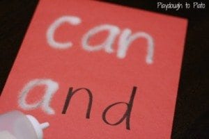 A child using a squeeze bottle of salt to trace words written on a card